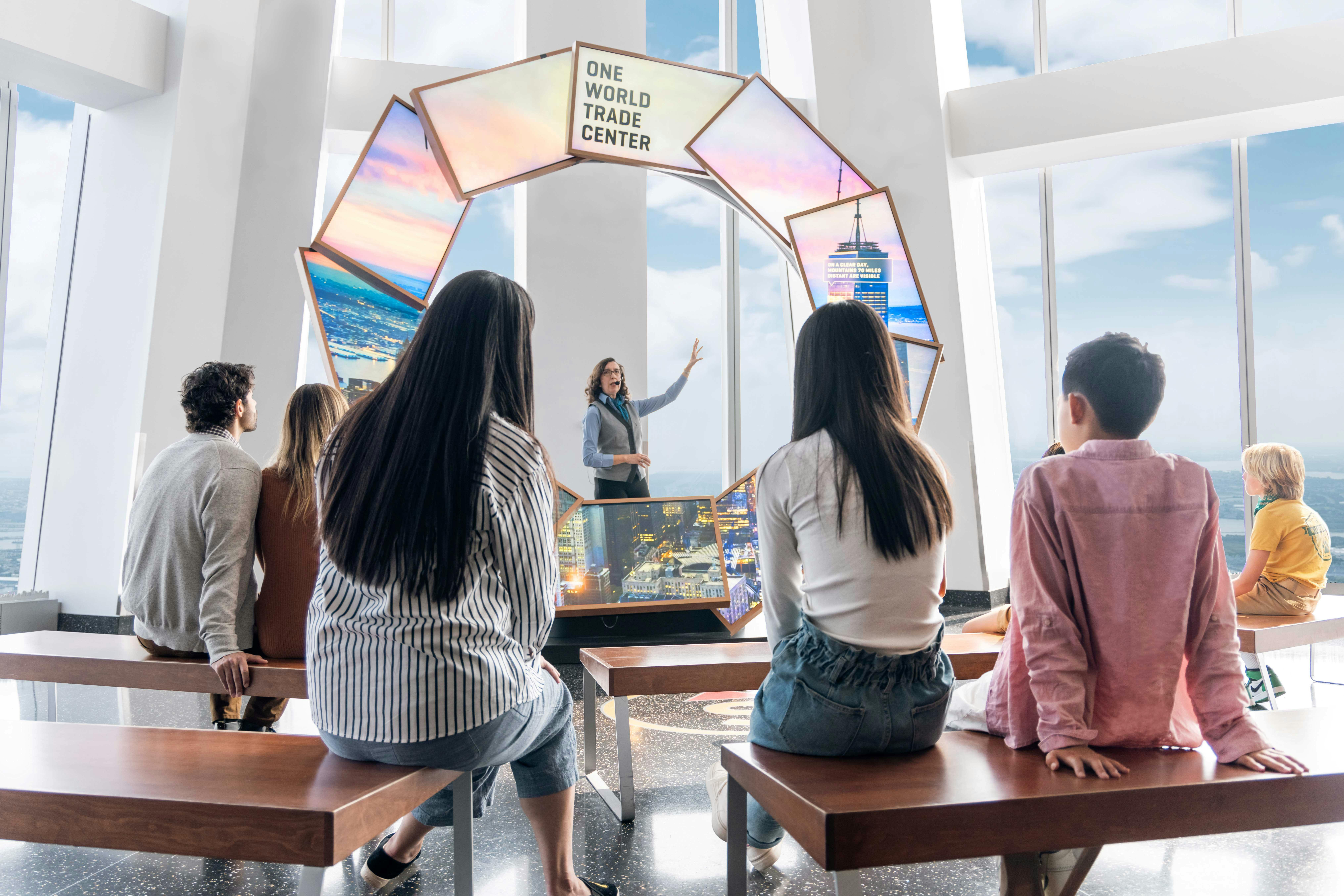 A guide speaking to a group of seated people in front of a display about One World Trade Center.