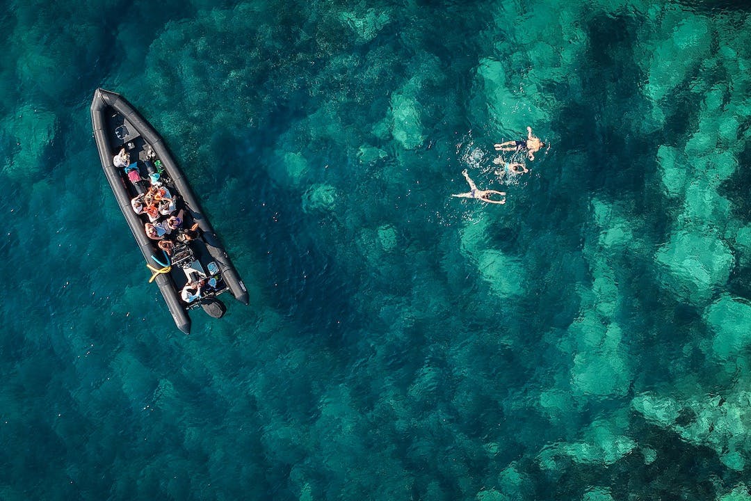 Människor som simmar i klart turkost vatten nära en båt med passagerare.