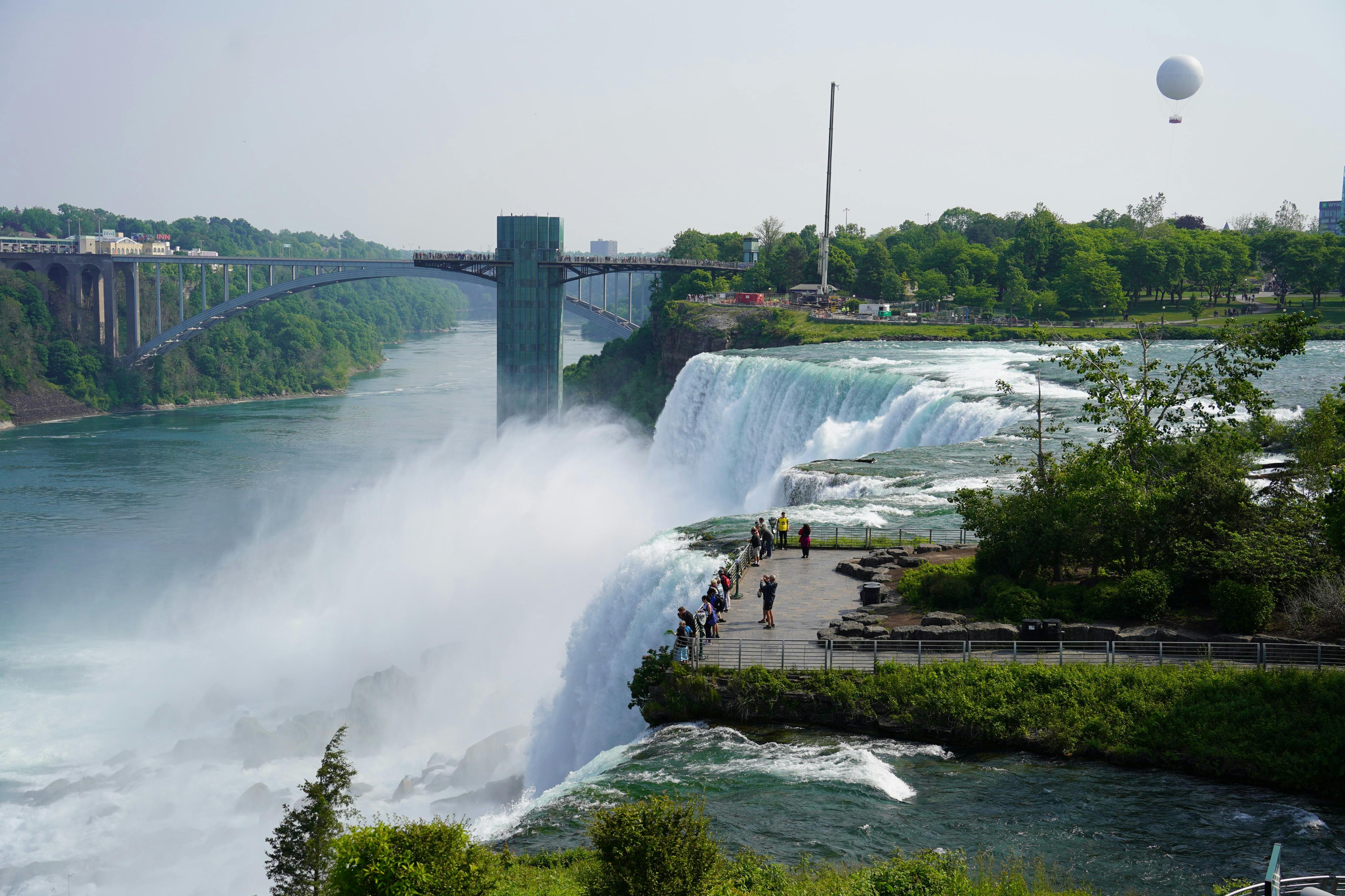 다리와 전망대를 배경으로 커다란 폭포 가장자리 근처의 전망대에 관광객들이 서 있습니다.