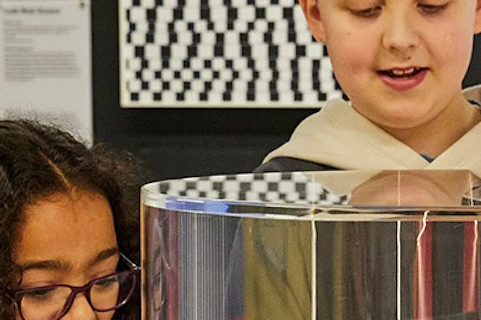 Two children interact with a glass-encased exhibit at a museum. One child looks surprised, and the other smiles.