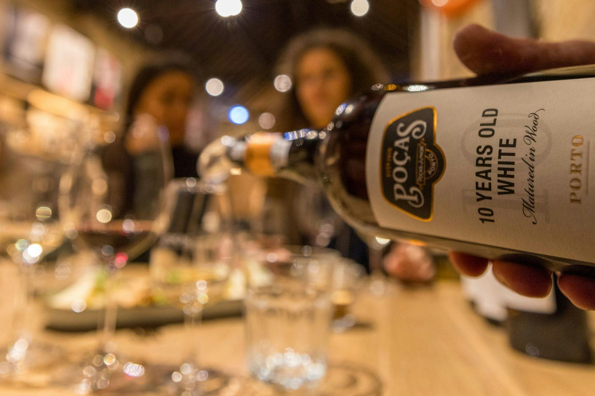 A bottle labelled '10 Years Old White' being poured at a table with blurred people and food in the background.