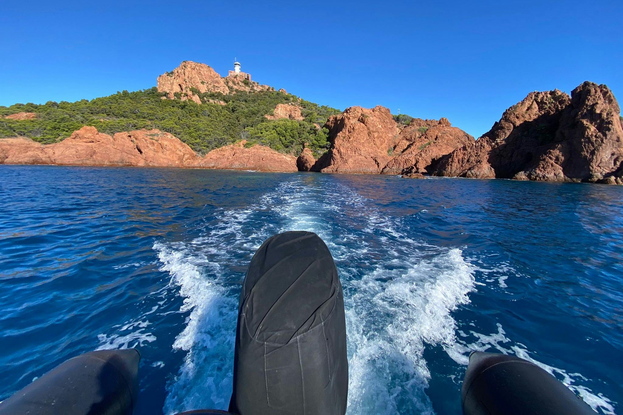 乘船在水面上欣赏美景，在晴朗的蓝天下，可以看到岩石海岸线和山顶上的灯塔。