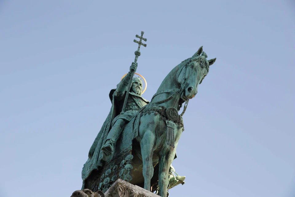 Bronze equestrian statue of a bearded figure holding a cross, on a stone pedestal, set against a clear blue sky.