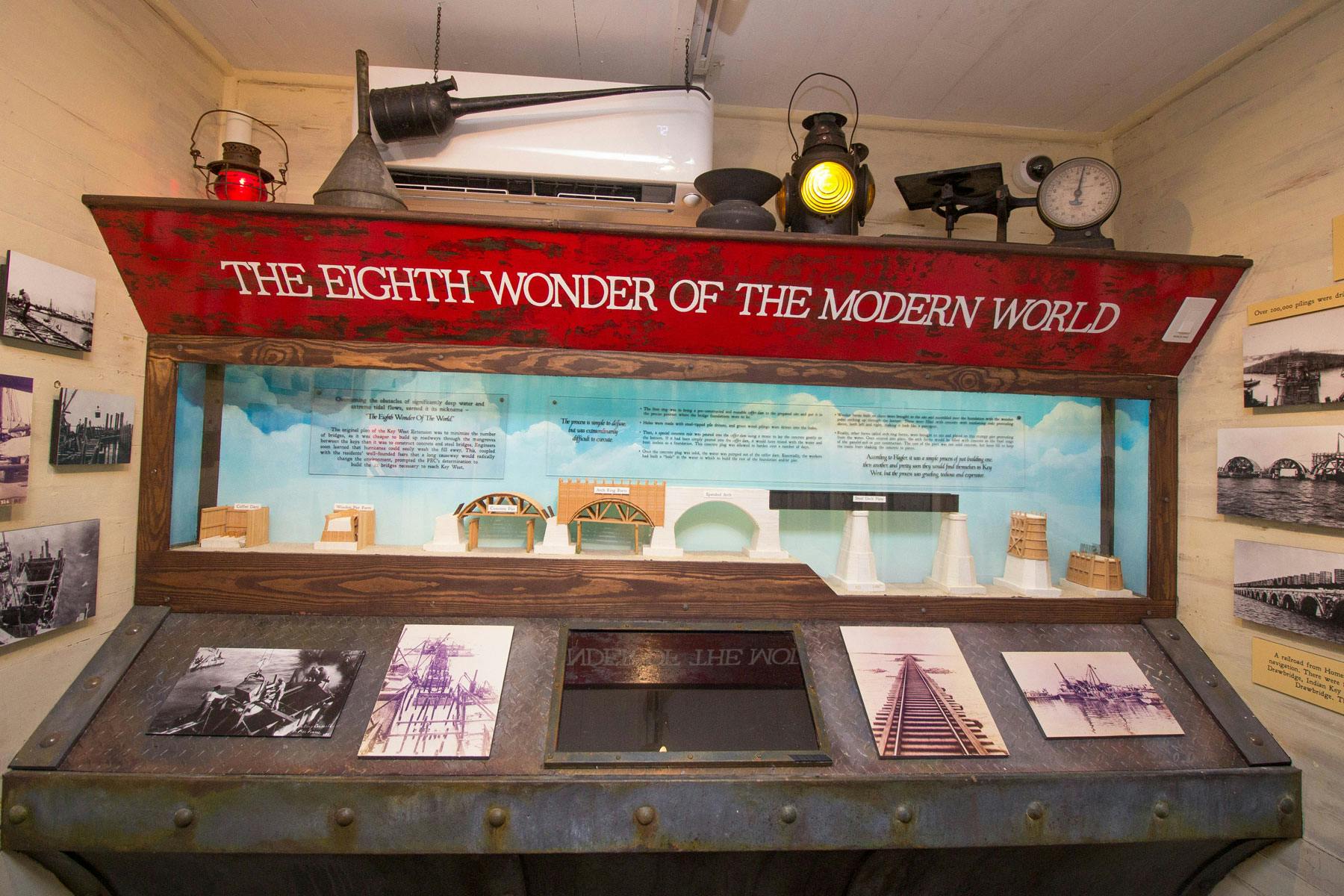 Utställning som visar historiska bromodeller och foton under en skylt med texten &#34;DEN MODERNA VÄRLDENS ÅTTONDE UNDERVERK&#34;.