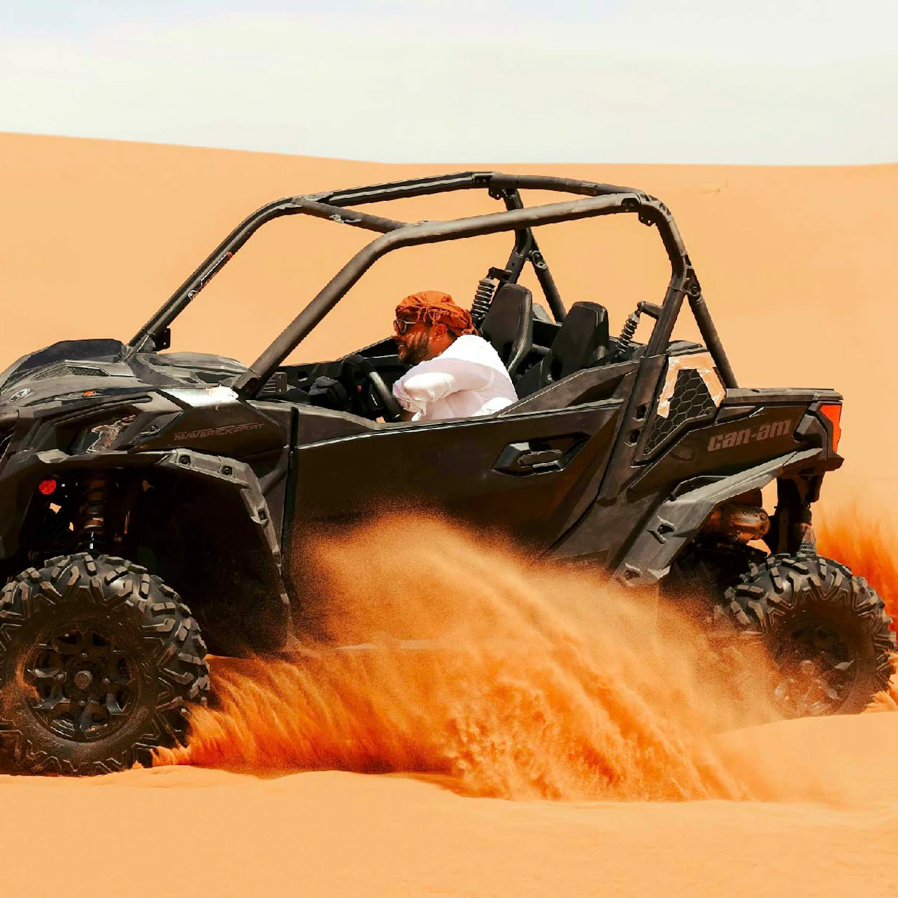 A person driving a black off-road vehicle through a sandy desert, with sand being kicked up by the tires.