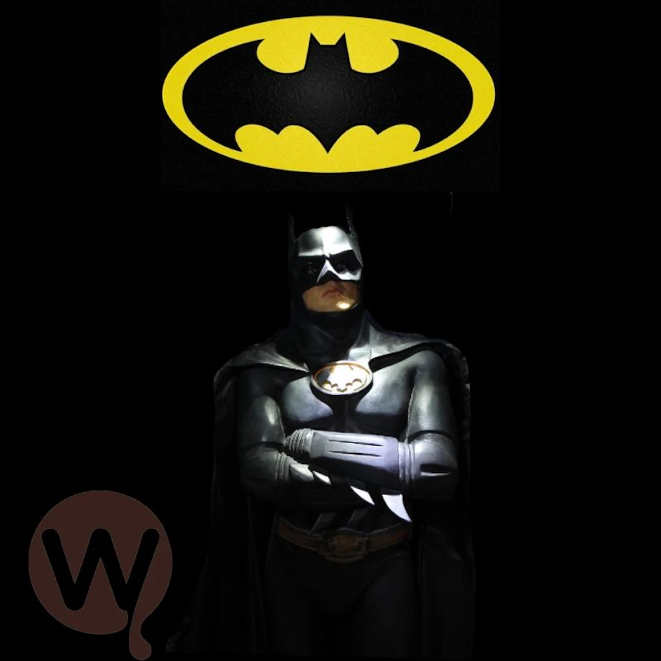 Person in a Batman costume stands with arms crossed, below a yellow Batman logo on a black background; a brown logo is in the bottom left corner.