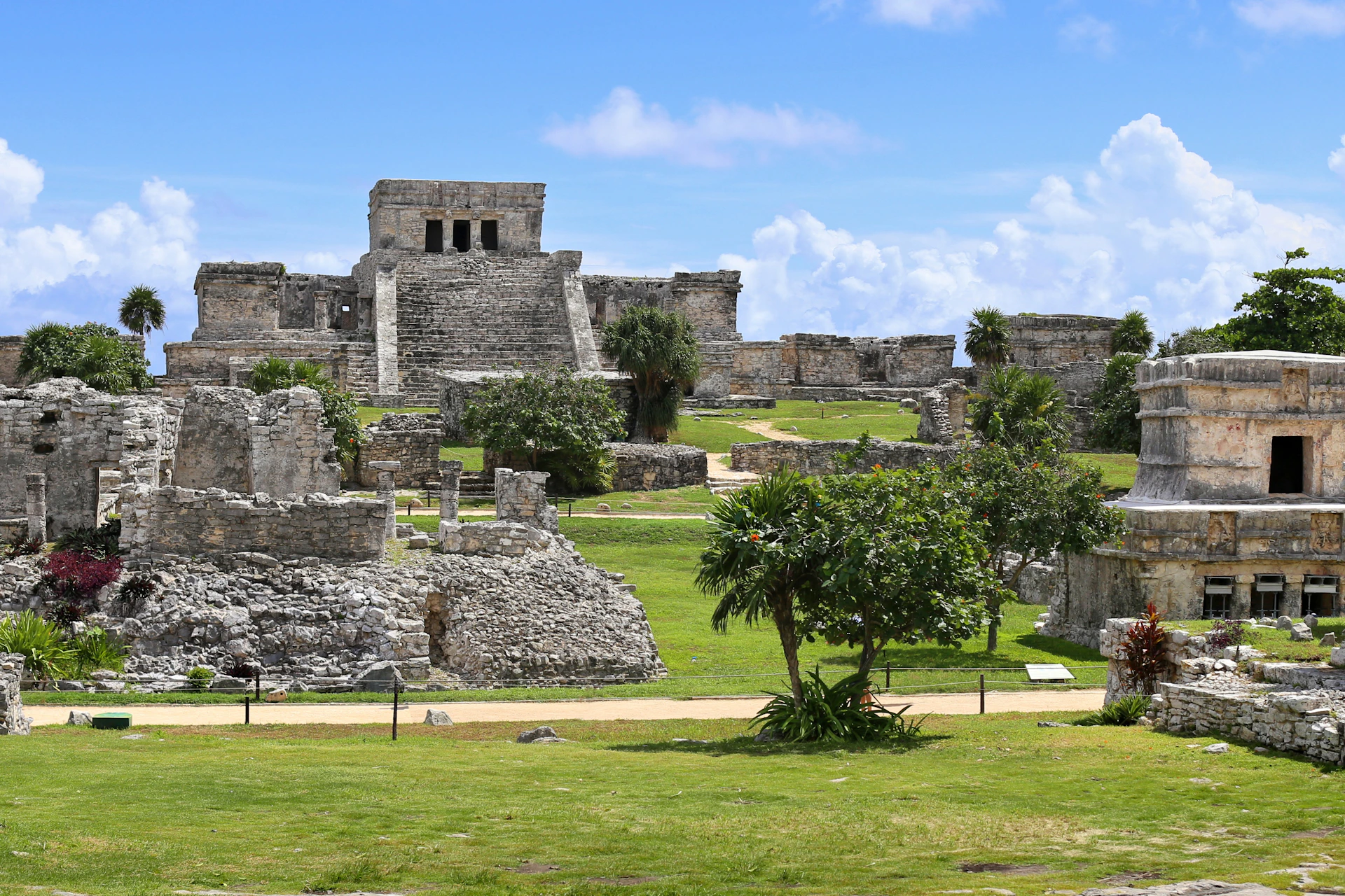 Ancient stone ruins with steps and lush green grass under a bright blue sky with scattered clouds.