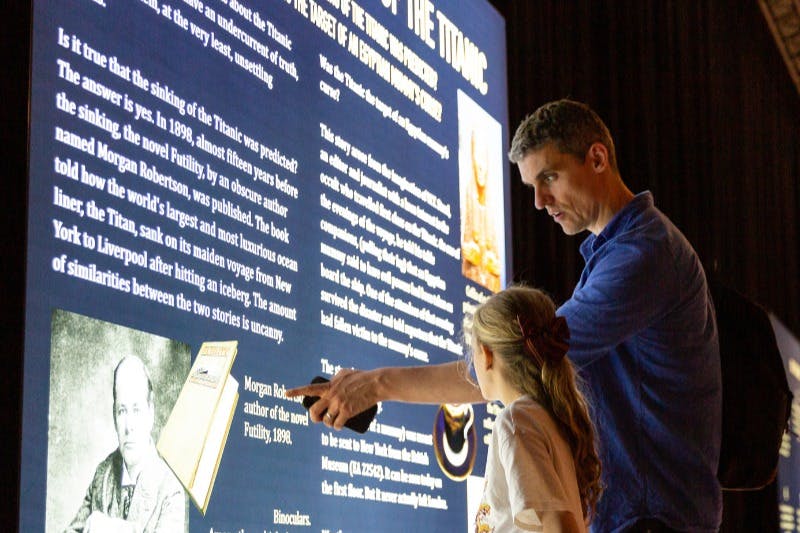 一个男人和一个女孩阅读并讨论关于泰坦尼克号的信息展示。 男子指着展览文字。