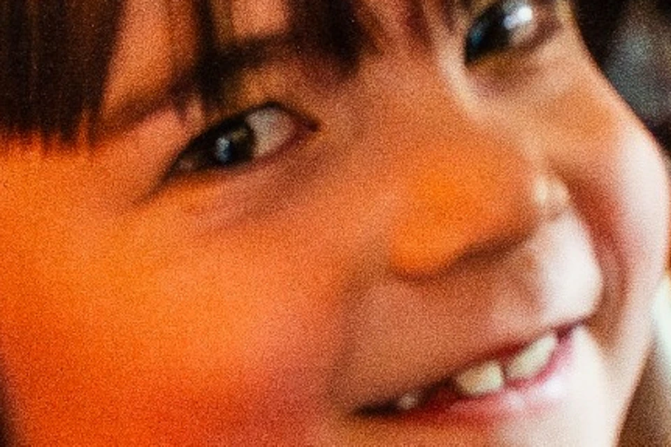 A child in a red hoodie smiles while holding a large wooden ship's wheel in a warmly lit interior.