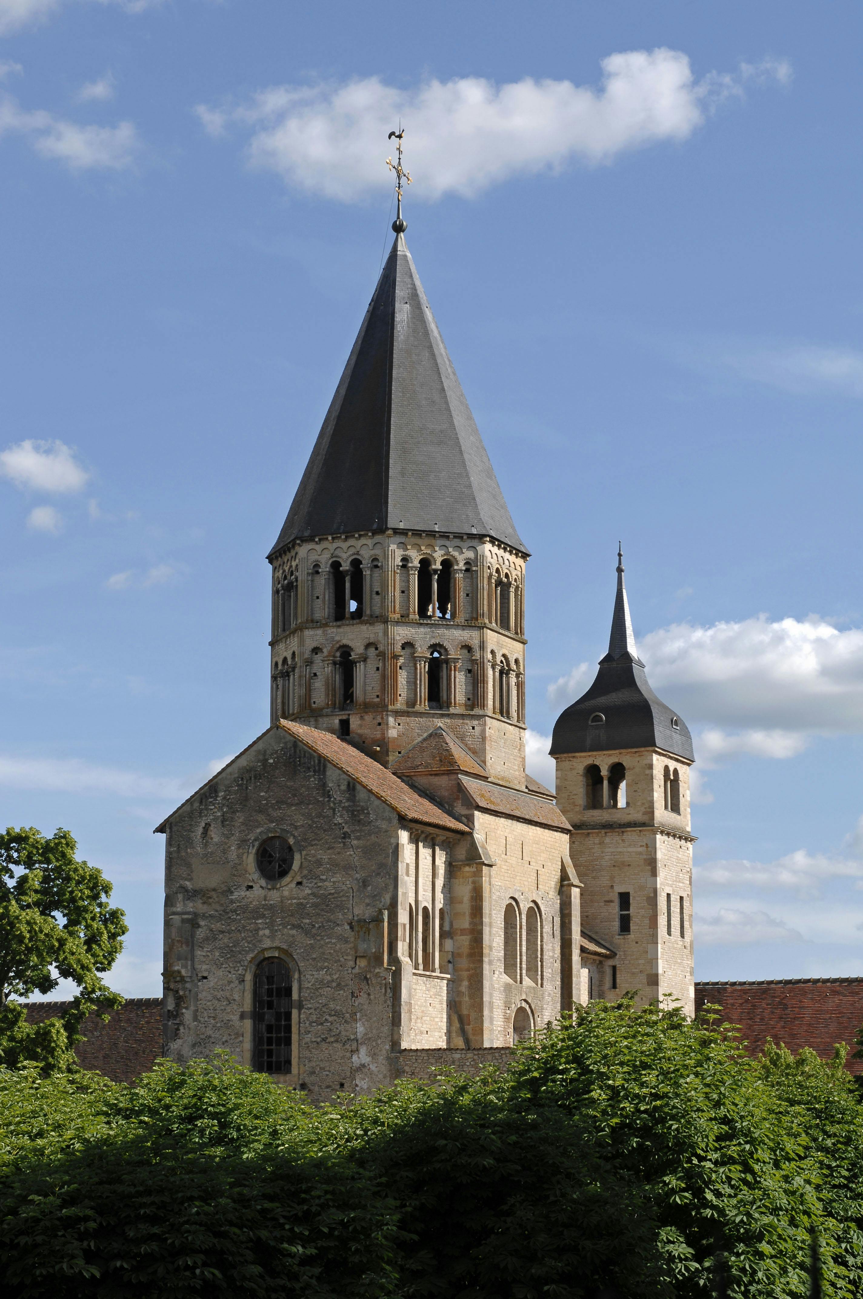 高く尖った中央塔と小さな丸い鐘楼を備えた石造りの教会は、青い空と数枚の雲を背景にしています。