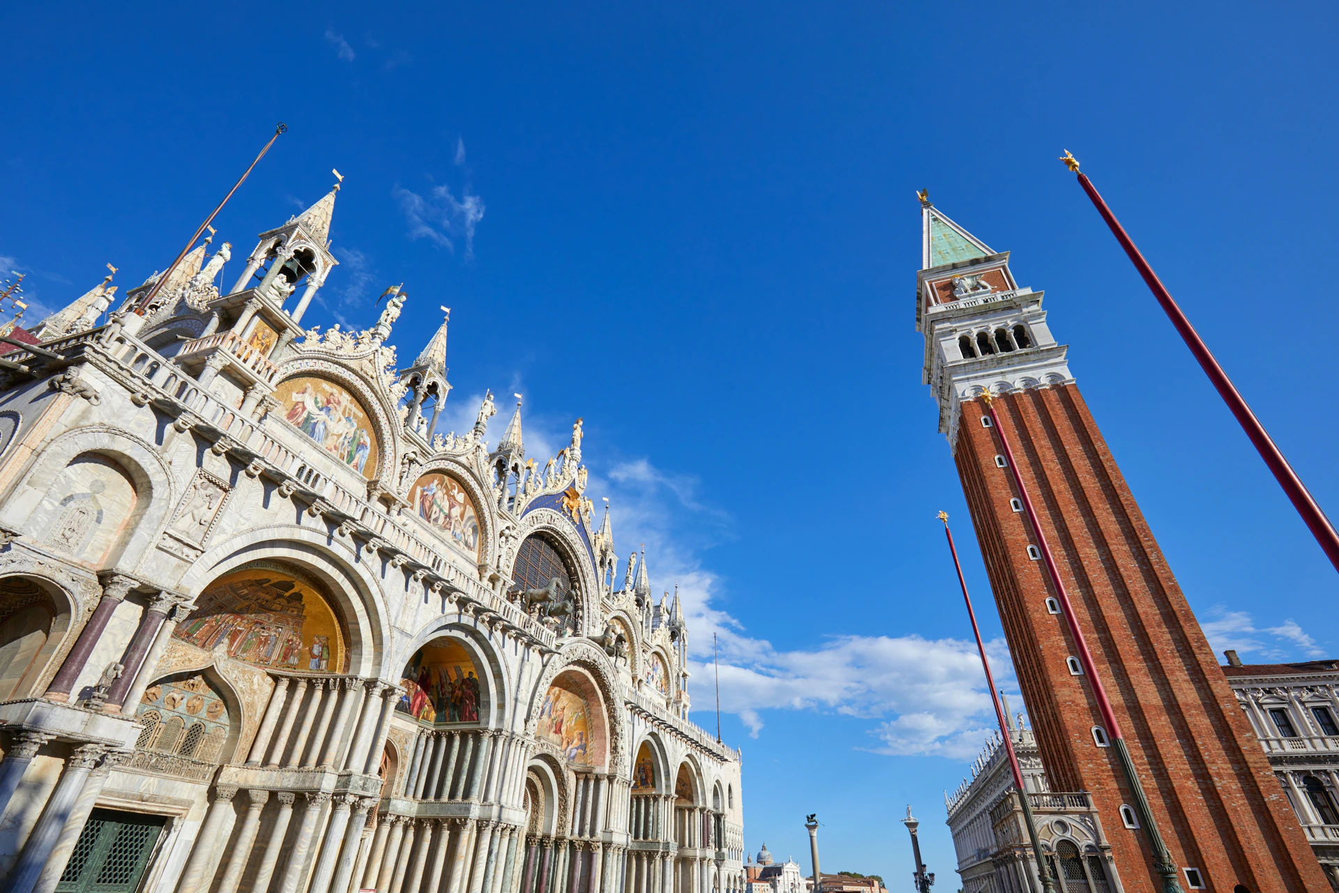 Ornate cathedral with arched windows and detailed carvings beside a tall, brick clock tower under a bright blue sky.