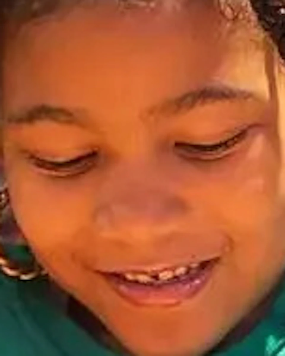 A child in a green shirt with a large "N" and name tag, Noor, is smiling while holding a stretchy yellow substance.