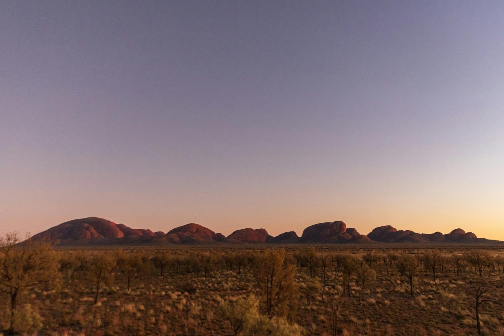 Una vista àmplia d'un paisatge desert amb llunyans turons rocosos al capvespre, sota un cel clar amb una sola estrella.