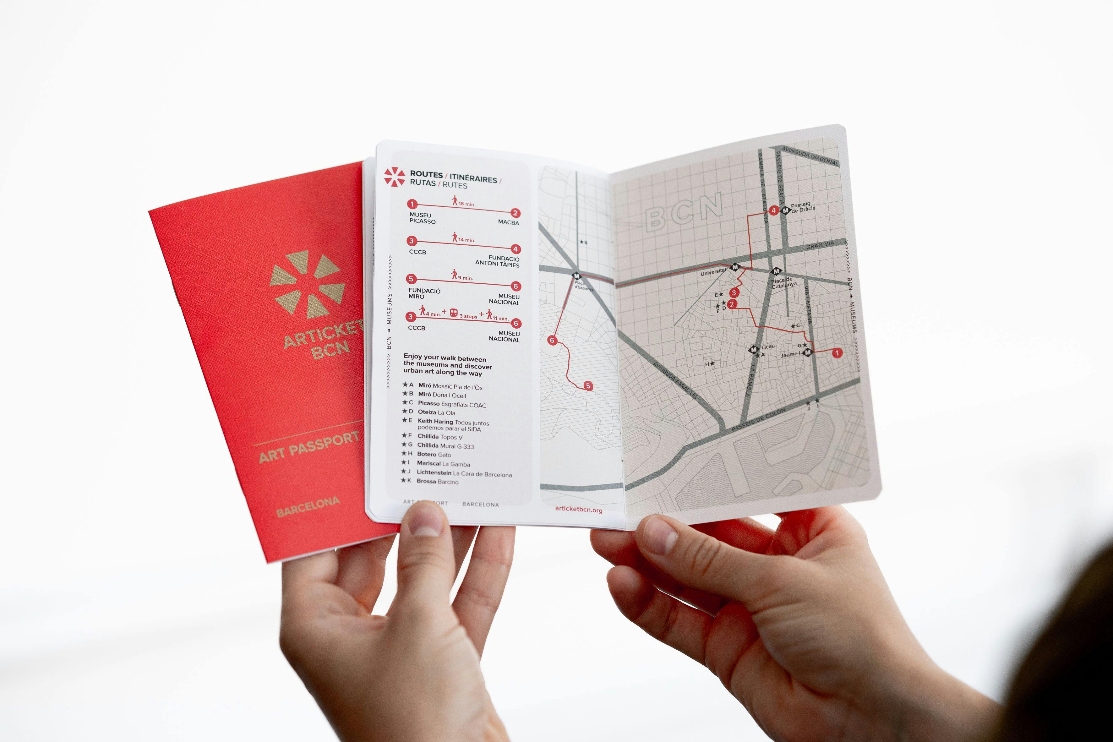 Hands holding an open passport with a red cover showing a map and itinerary to various art locations in Barcelona.