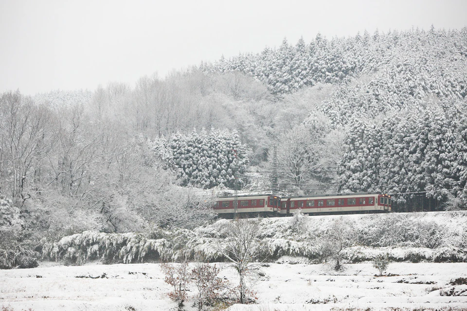 A red train traveling through a snowy forest landscape, with snow-covered trees and ground.