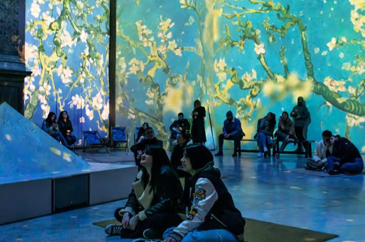 Persone sedute e in piedi in una stanza con immagini proiettate dei fiori di mandorlo di Vincent van Gogh sulle pareti.