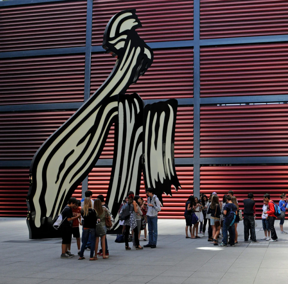People gathered in front of a large abstract black and white sculpture, set against a background of red horizontal panels.
