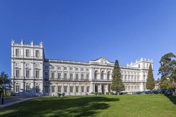 宽敞的白色新古典主义建筑，有多扇窗户和一个宏伟的入口，坐落在晴朗的蓝天下修剪整齐的草坪上。