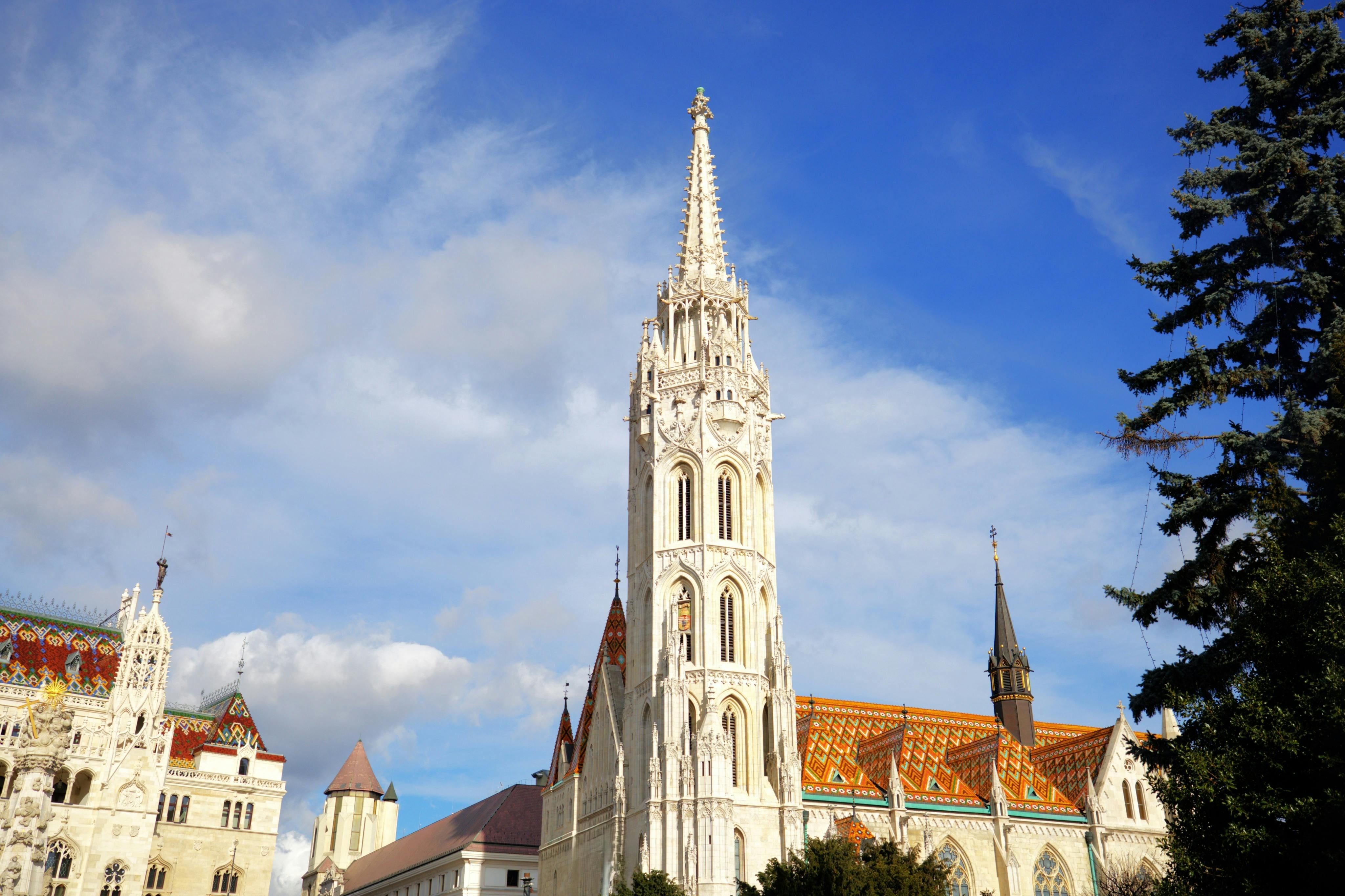 A tall, ornate church tower with colorful tiled roof under a blue sky with scattered clouds.