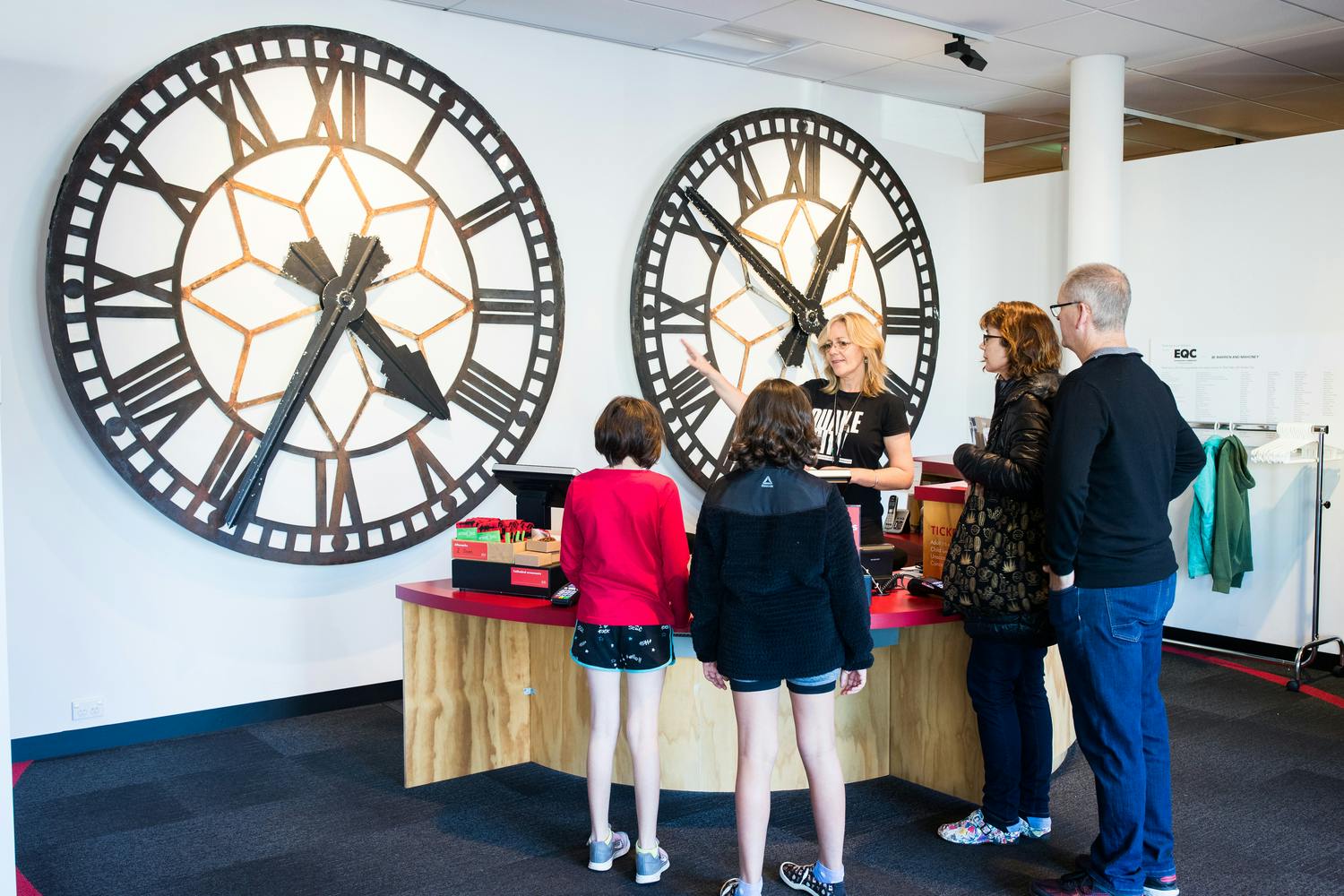 A group of people standing in a museum exhibit featuring large clock faces and a display table.