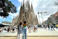 Besøgende, der beundrer den majestætiske facade af Sagrada Familia i Barcelona på en solskinsdag.