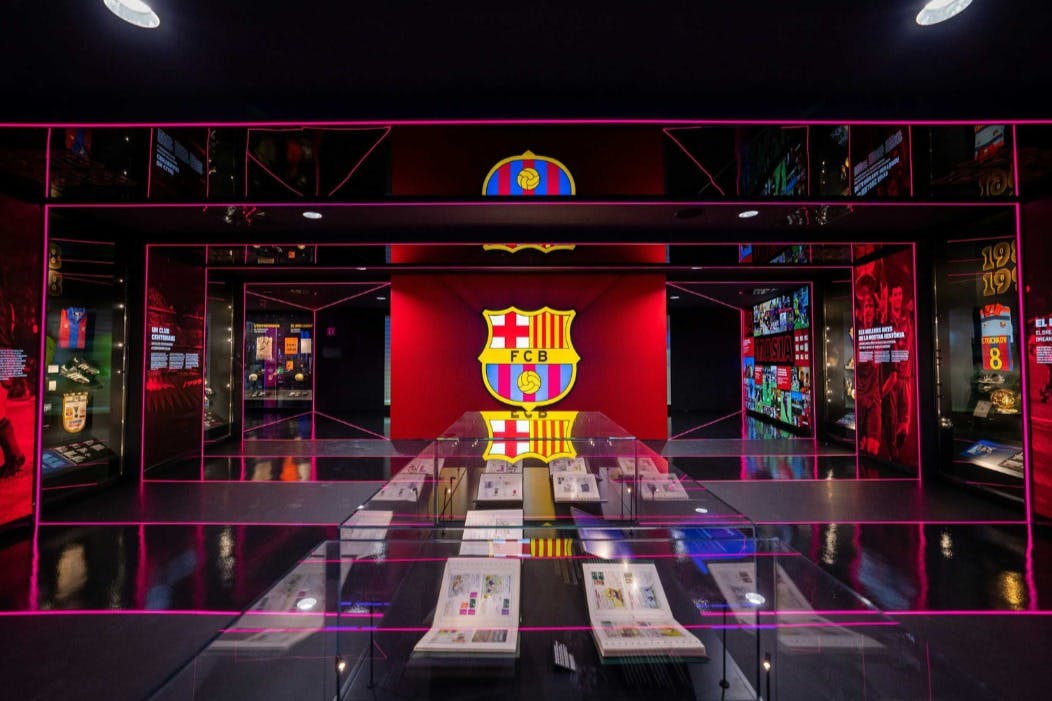 Een museum tentoonstelling met Barcelona FC emblemen, verlichte displays en glazen vitrines met documenten op een glanzende vloer.