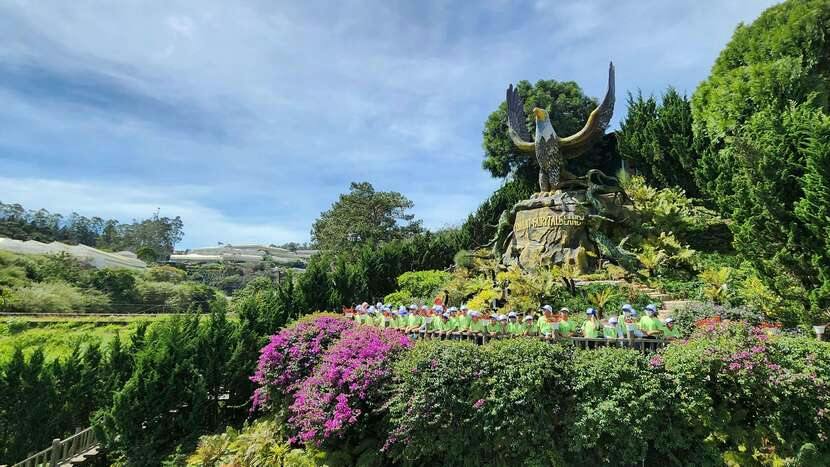 A large eagle statue on a landscaped hill surrounded by flowers and greenery, with a group of people in front.