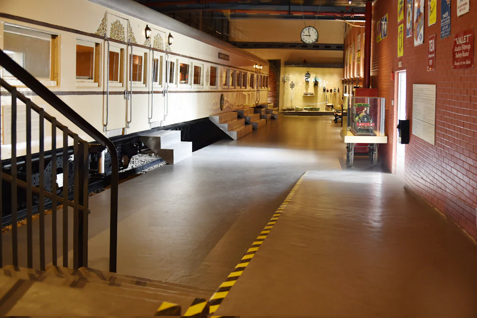 An indoor exhibit featuring a vintage train car on the left and a well-lit display area with various artifacts on the right.