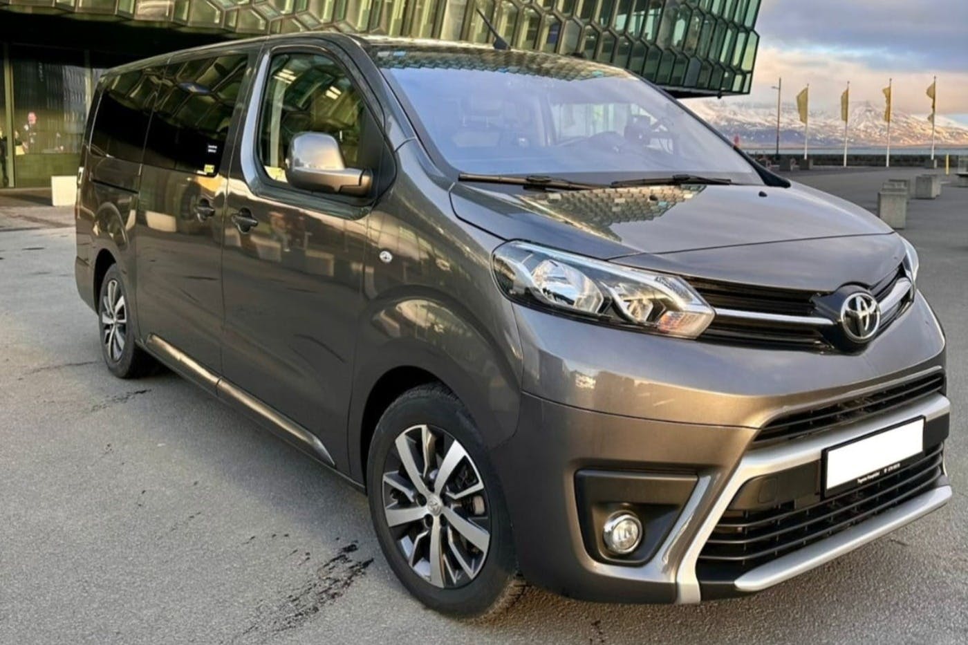 Gray minivan parked on a street with a modern glass-front building in the background.