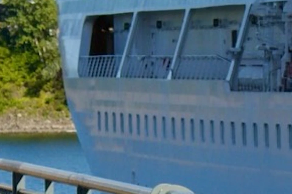 A person playing mini-golf on an outdoor course by a river, with a large ship docked in the background.