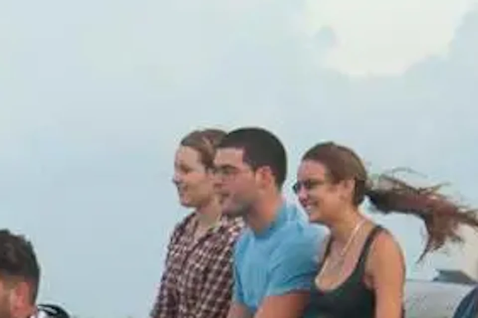 A group of people seated on an airboat gliding through marshland, with a person steering and a red flag on the boat.