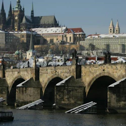 Ett snötäckt Prag med Karlsbron i förgrunden och stadens gotiska arkitektur i bakgrunden under en klar himmel.