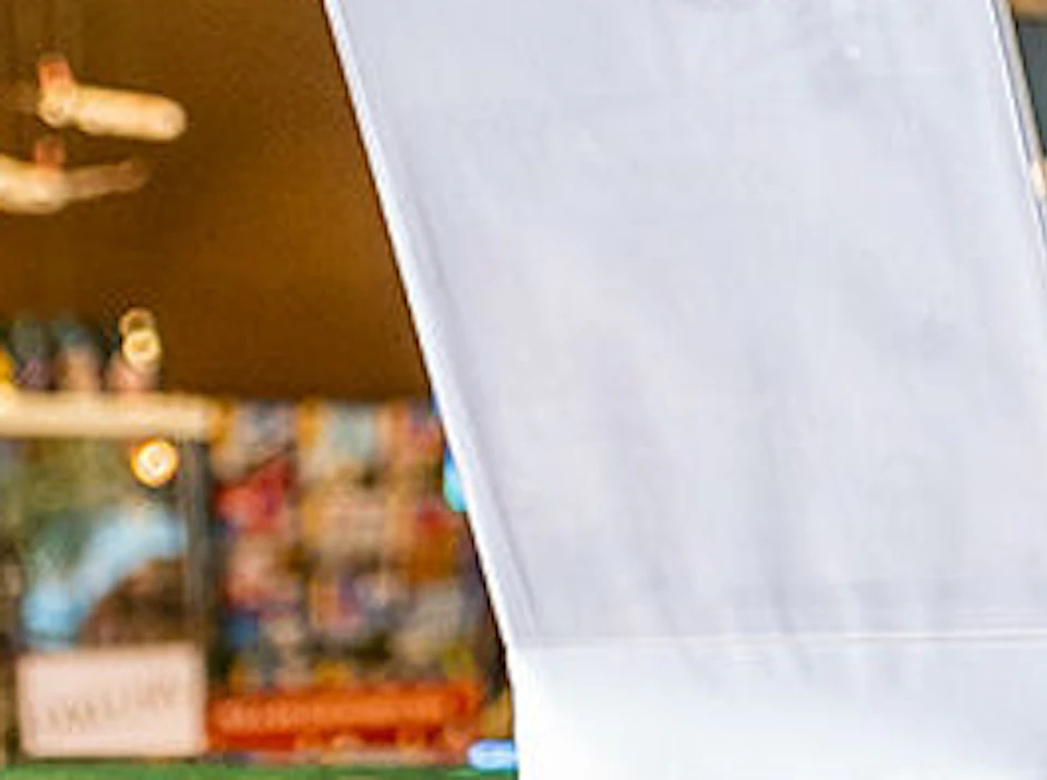 A chef in a white uniform and hat serves a chocolate sample to a customer in a brightly lit shop.