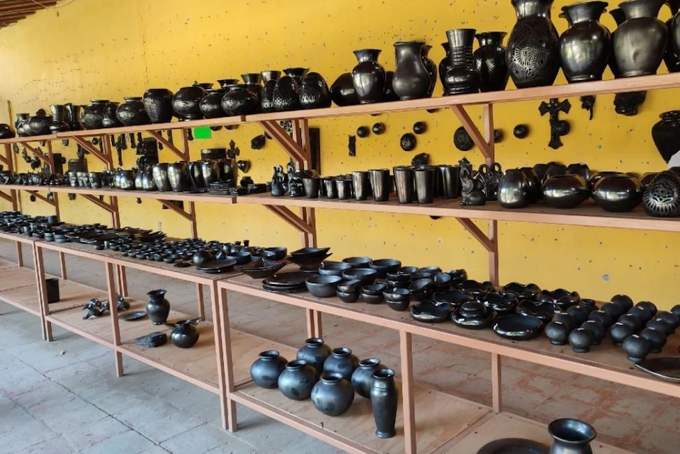 Shelves displaying a variety of black ceramic pottery pieces against a yellow wall.