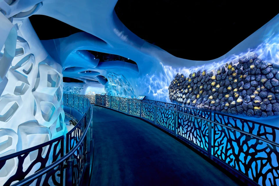 A blue-themed aquarium tunnel with decorative railings, rock formations, and illuminated water-like textures on the walls.