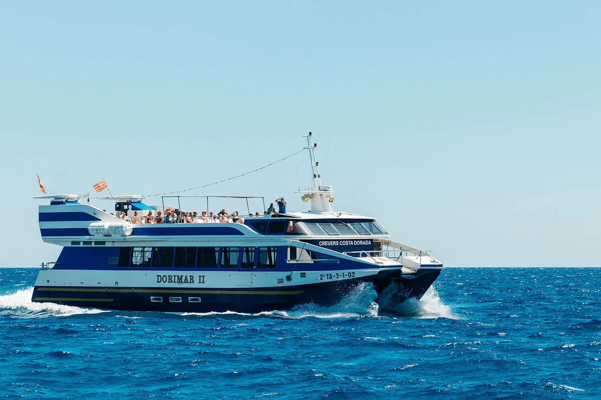 A passenger ferry named Dorimar II sailing on clear blue water under a sunny sky, with people visible on its upper deck.