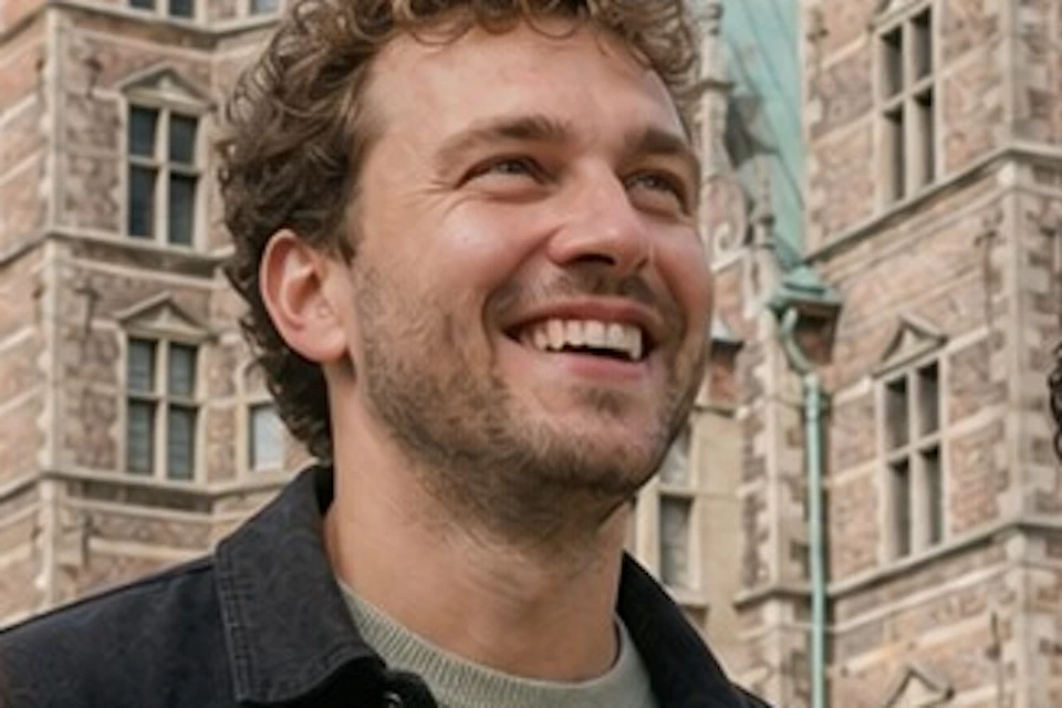 Three people smiling while standing in front of a historic building with green spires on a bright day.