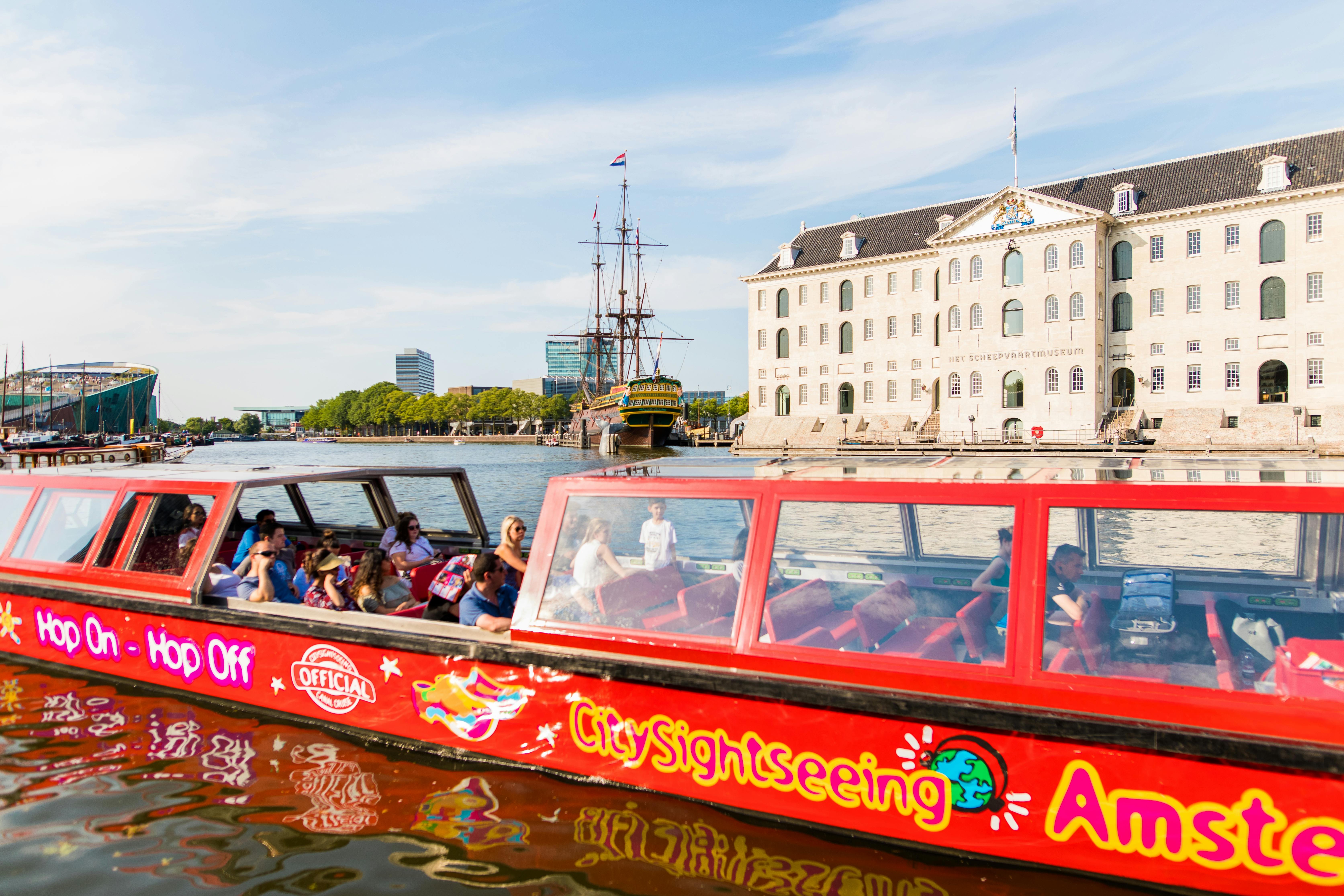 암스테르담의 Het Scheepvaartmuseum 앞에는 관광객으로 가득한 붉은 도시 관광 보트가 운하에 있습니다.