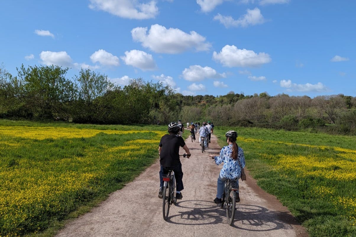 A group of people riding bicycles on a path through a scenic, grassy area under a blue sky with fluffy clouds.