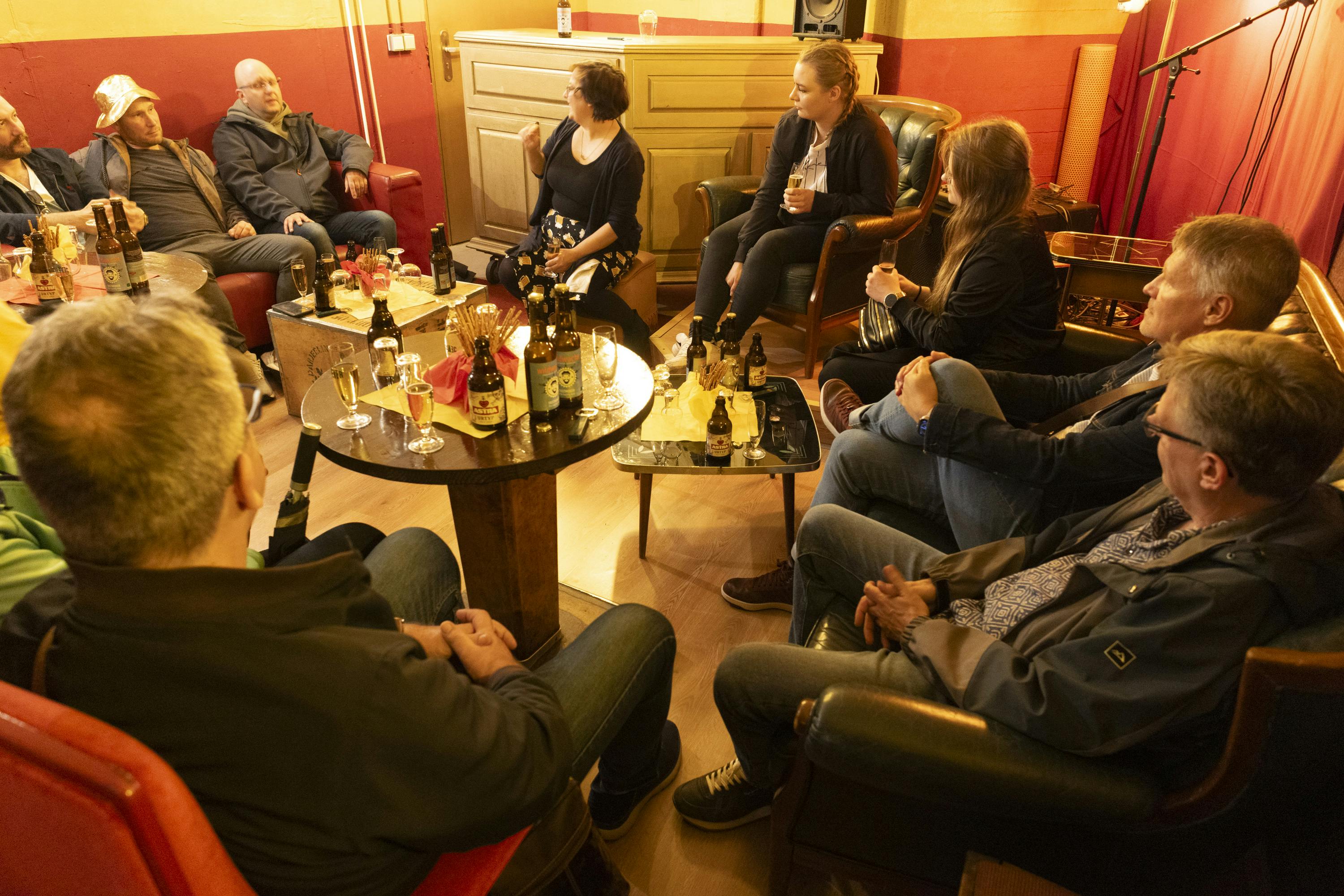 Folk sidder i et hyggeligt rum og sludrer og drikker, med flasker og glas på bordene.