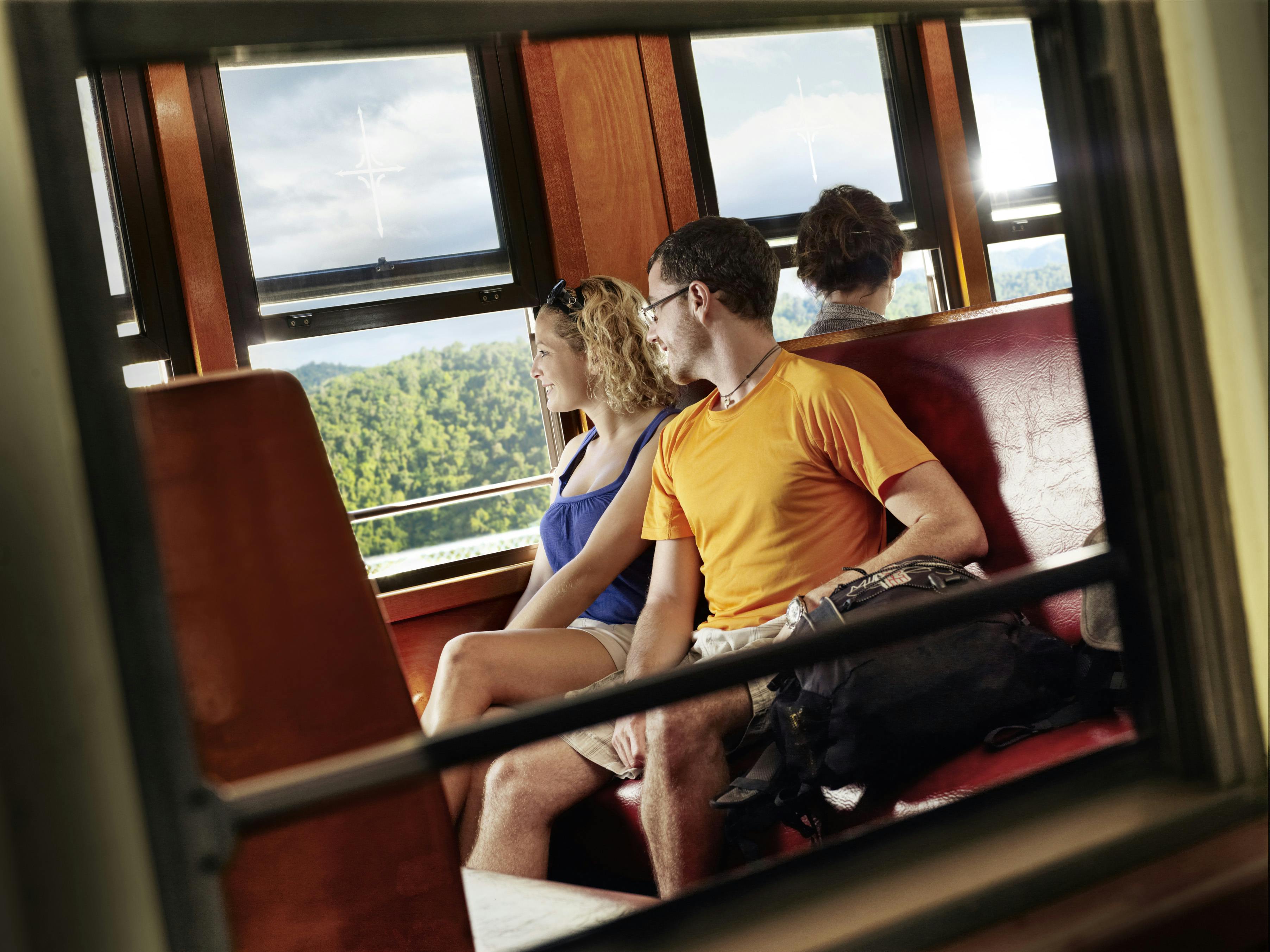 A man and a woman sit together on a train, looking out the window at the scenic mountain view.