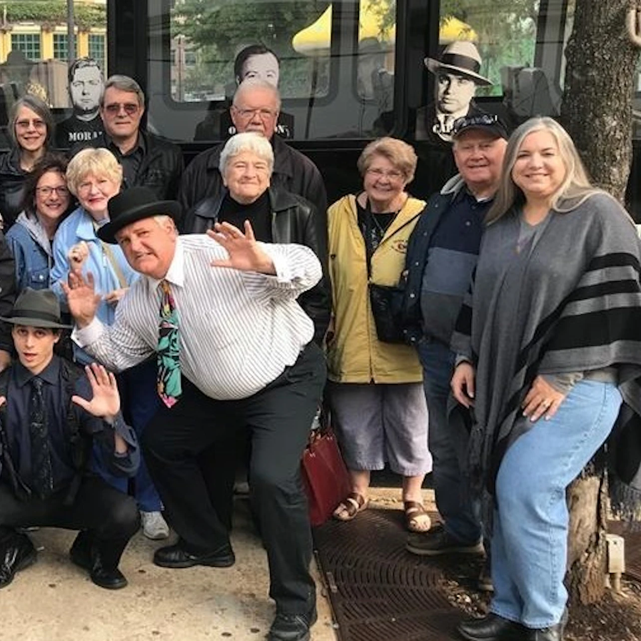 A group of people poses together on a sidewalk in front of a bus with pictures of faces in the windows.