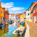 Colorful buildings line a canal with boats moored along the sides under a clear, blue sky.