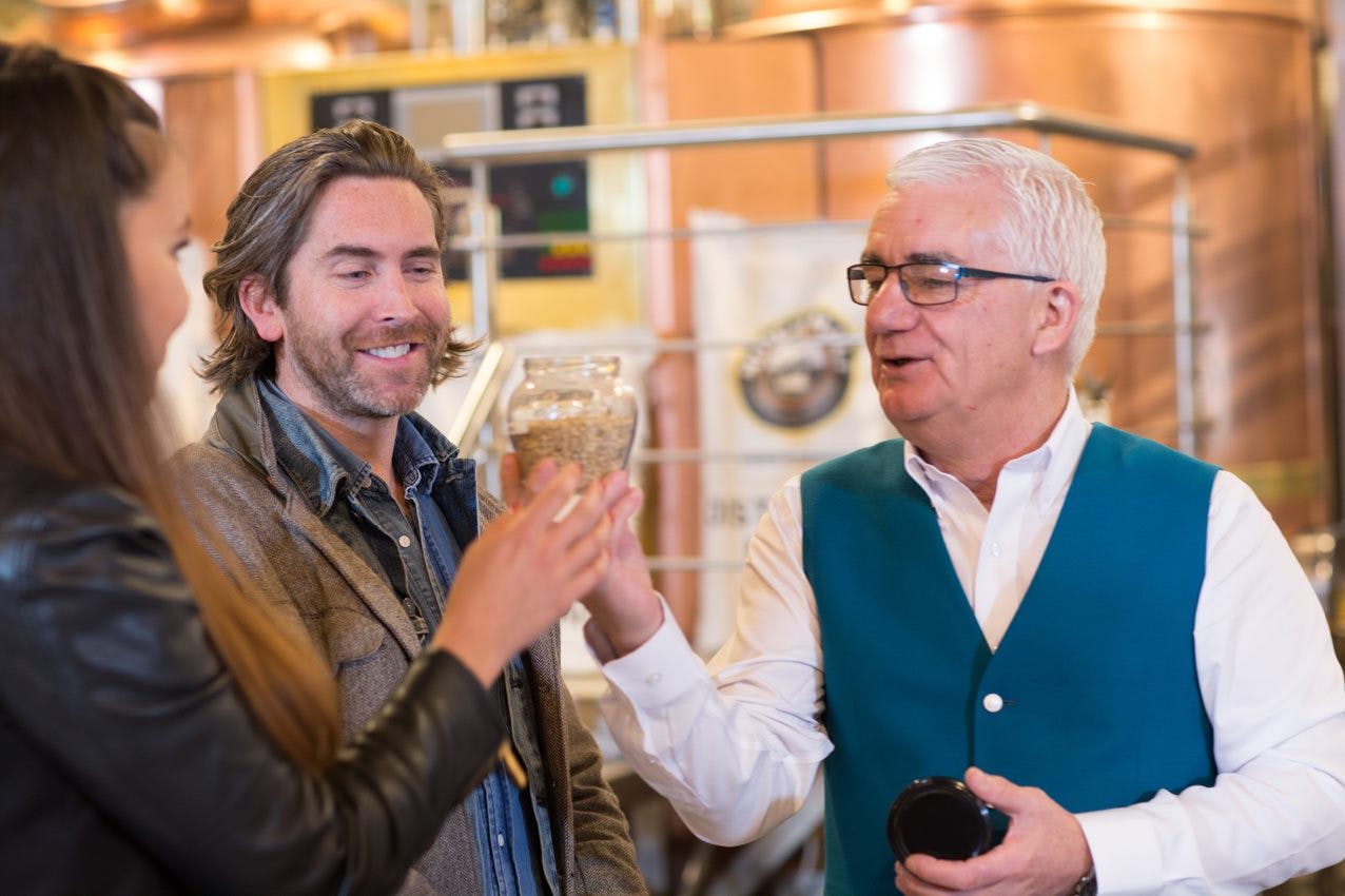 暖かく照らされた屋内で、3人が穀物の瓶を持って微笑んでいます。