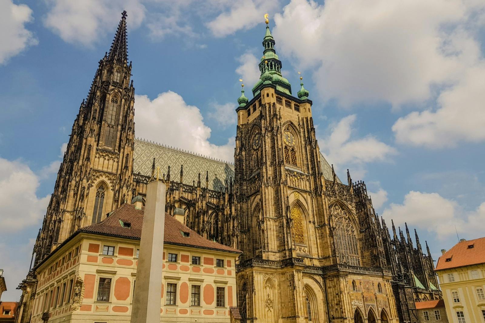 Gothic-style cathedral with tall spires and ornate detailing, adjacent to a colorful building, against a partly cloudy sky.