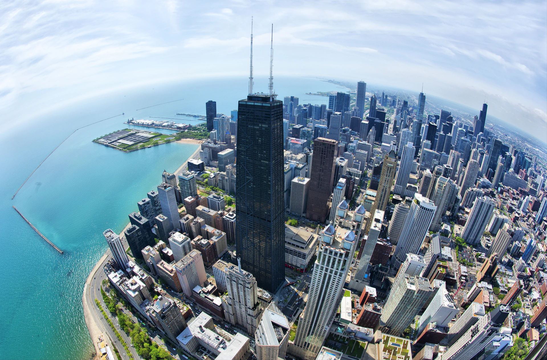 Aerial view of a city skyline featuring tall buildings, with a large body of water and a park area in the background.