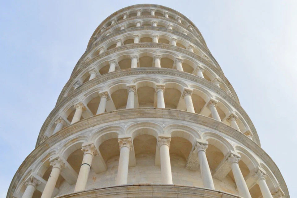 Upward view of the Leaning Tower of Pisa, showing its circular balconies and columns against a clear sky.