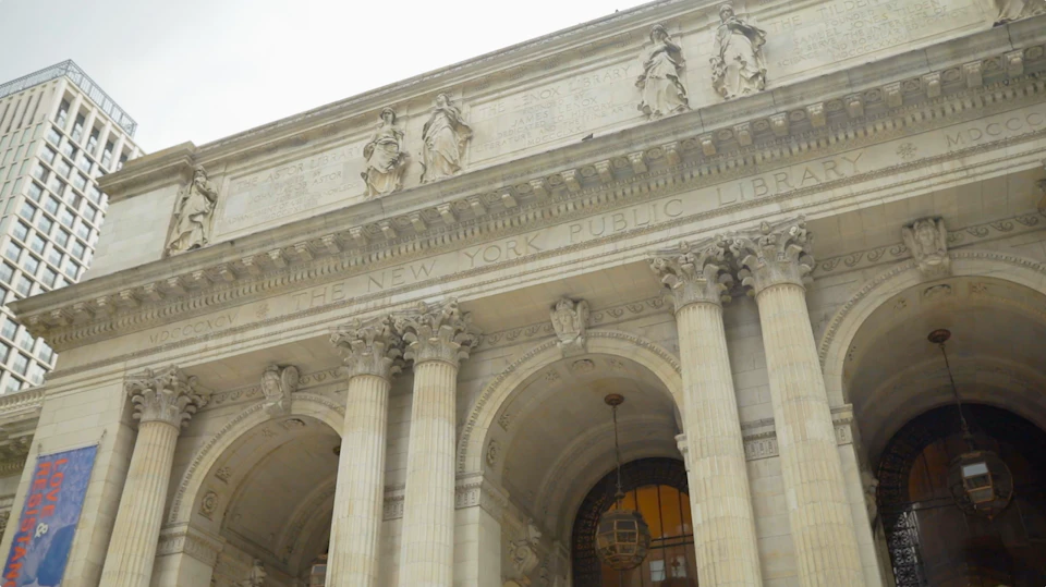 Facade of the New York Public Library featuring columns, statues, and architectural details under a cloudy sky.
