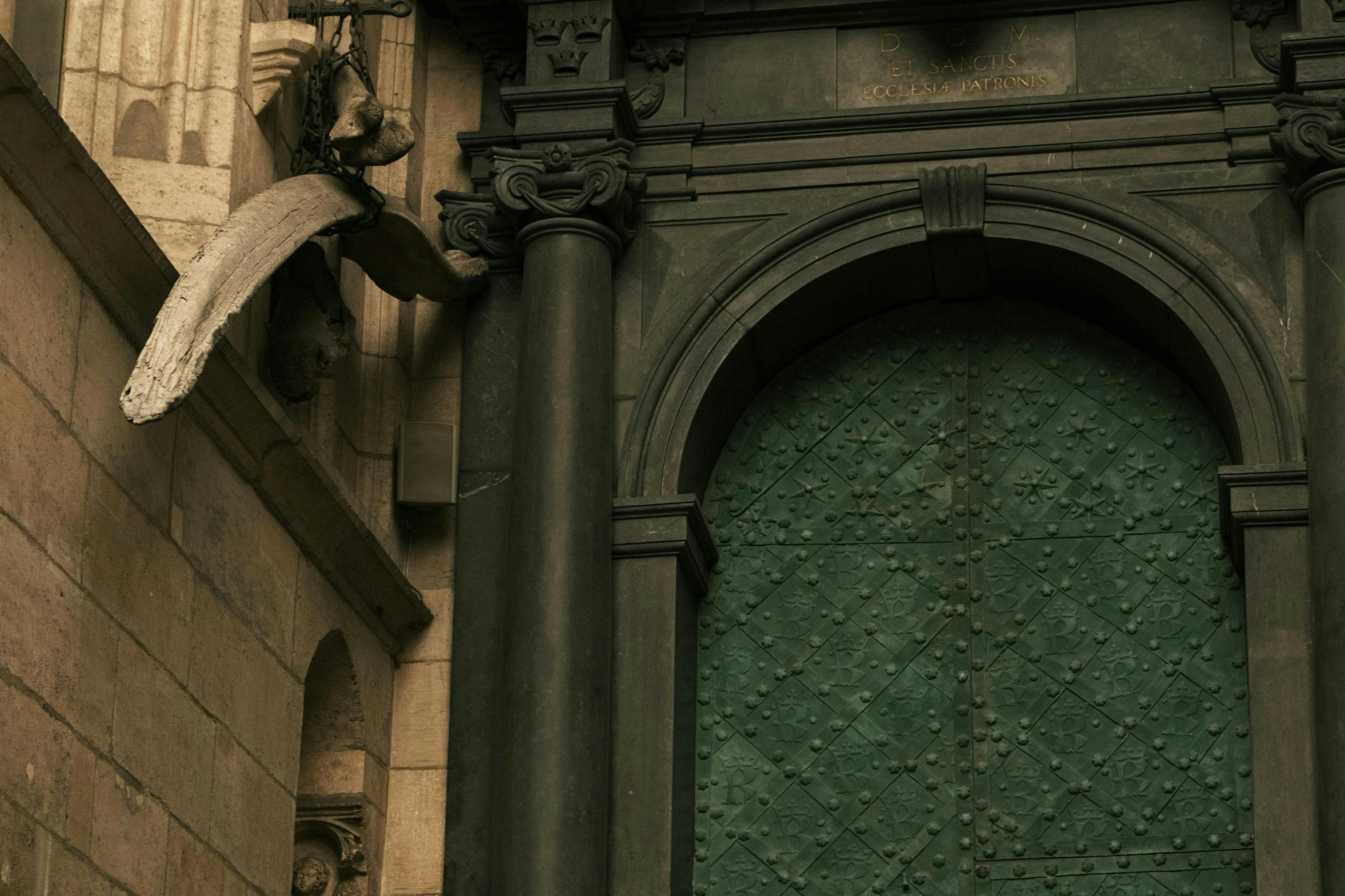 一扇大型绿色拱形门，饰有华丽的石头细节，侧面有一根柱子。