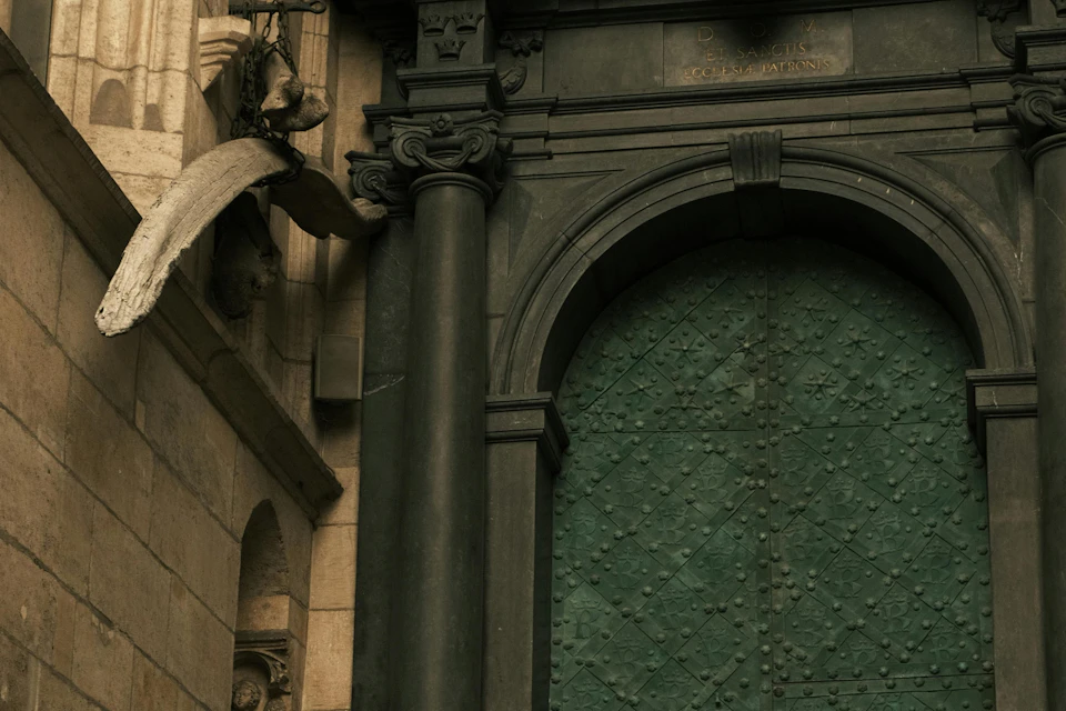 A close-up view of a large green arched door with ornate stone details and a column on the side.